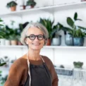 Portrait of senior female florist at small business flower shop. Happy mature woman wearing apron working in a small flower store.